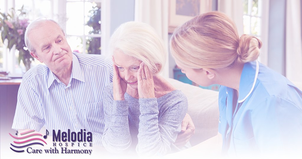 Elderly woman and her husband sitting sadly on sofa with hospice nurse