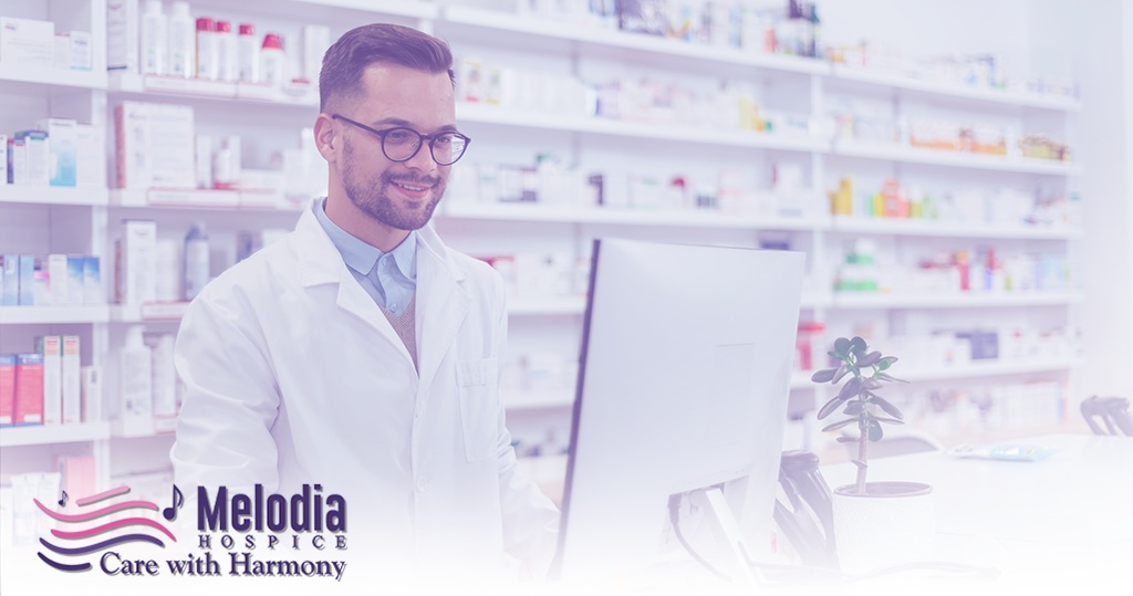 Pharmacist working on a computer in a pharmacy, supporting palliative care services