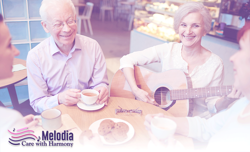 Elderly individuals enjoying tea and cookies while participating in hospice music therapy session led by woman playing guitar